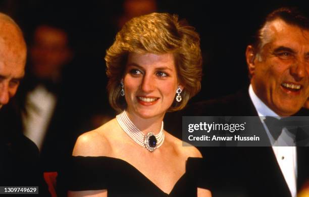 Diana, Princess of Wales, wearing a midnight blue velvet, off the shoulder evening dress designed by Victor Edelstein, a sapphire, diamond and pearl...