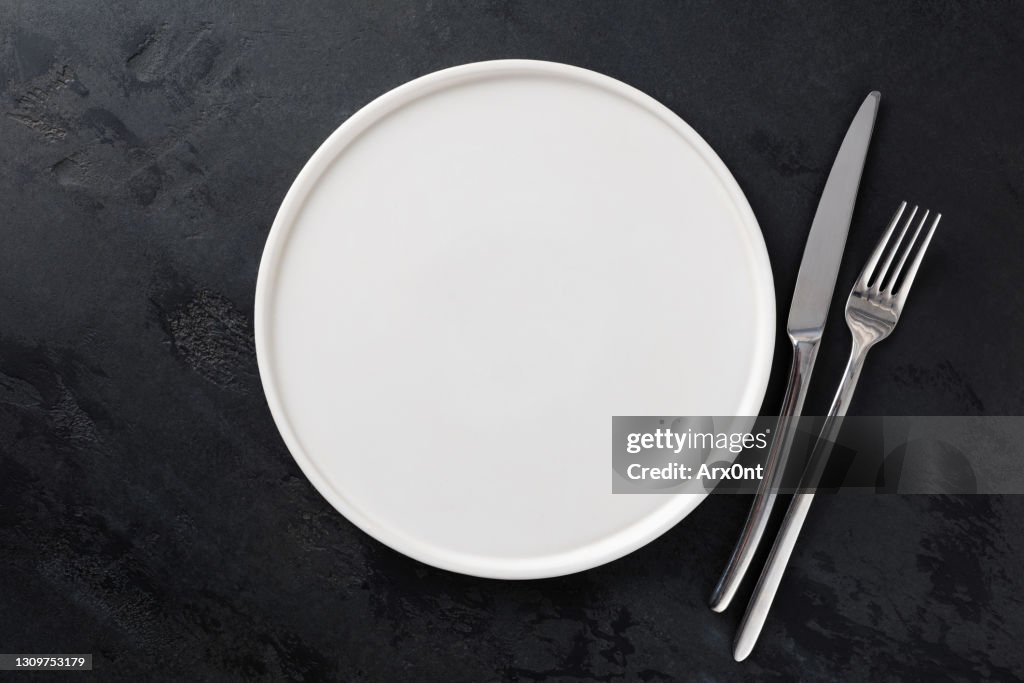 Empty white plate and silver cutlery on black background