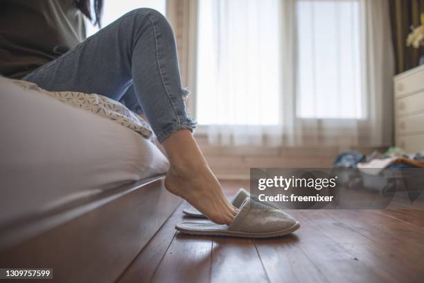 primer plano de los pies de la mujer mientras se sienta en la cama y se pone zapatillas - jeans barefoot fotografías e imágenes de stock