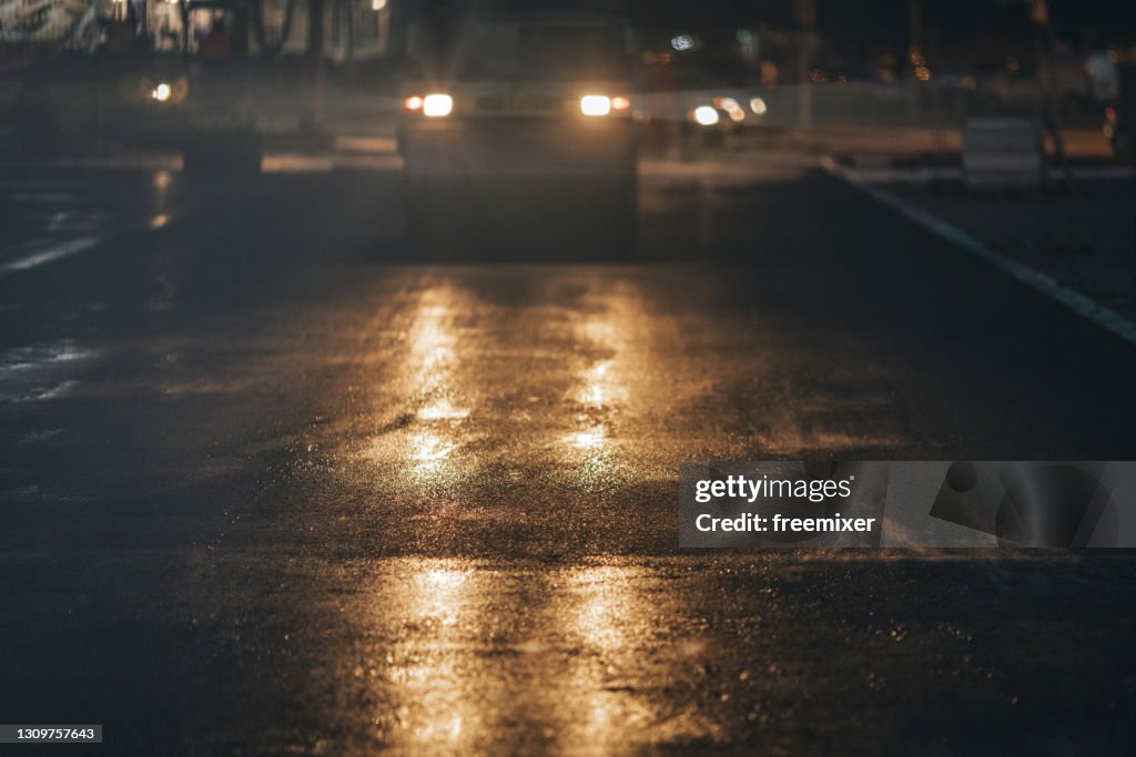 Steamroller compacting asphalt on city street at night