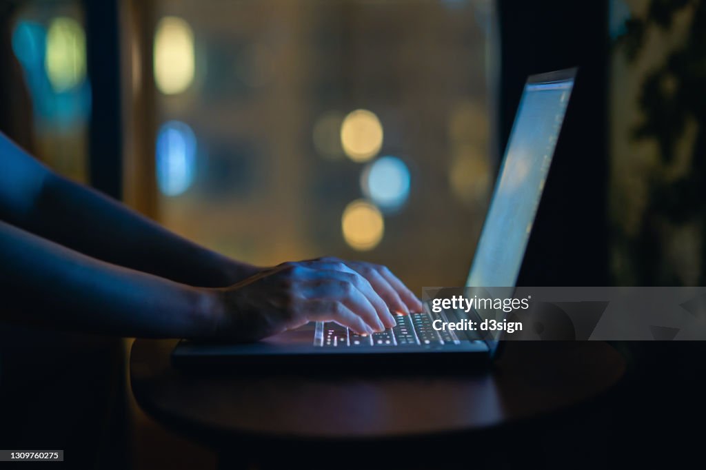 Cropped shot of woman's hand typing on computer keyboard in the dark, working late on laptop at home