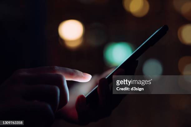 close up of woman's hand using smartphone in the dark, against illuminated city light bokeh - alone office night stockfoto's en -beelden