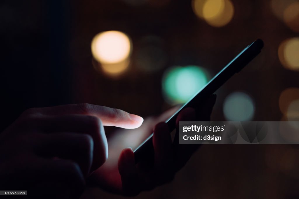 Close up of woman's hand using smartphone in the dark, against illuminated city light bokeh