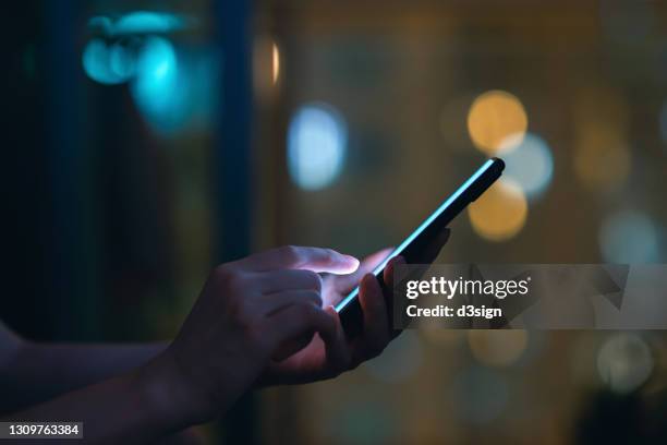 close up of woman's hand using smartphone in the dark, against illuminated city light bokeh - computer hacker stockfoto's en -beelden