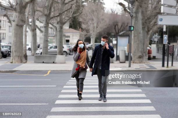 una joven pareja enmascarada cruza una calle en un paso de peatones mientras telefonea - activité avec mouvement fotografías e imágenes de stock