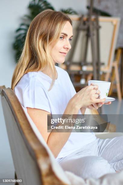 young woman sits with a hot drink, watching out of the window from the comfort - enjoying coffee cafe morning light stock pictures, royalty-free photos & images