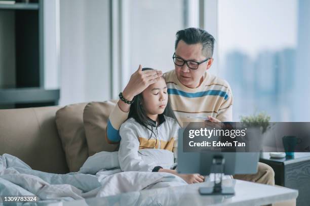 aziatische chinesse vader nemen temperatuur voor zijn zieke dochter op bank woonkamer videocall met zijn arts via digitale tablet - medical examination room stockfoto's en -beelden