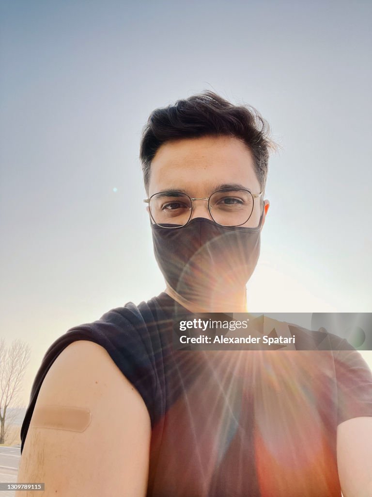 Young man taking a selfie with band-aid on shoulder after getting vaccine for COVID-19