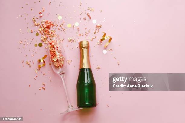 champagne bottle and glass with golden confetti and glitter over pink background. flat lay. concept of party and celebration. - exploding glass stockfoto's en -beelden