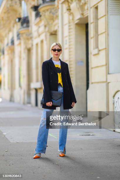Emy Venturini @sustainably_by_emy wears sunglasses, a black long jacket from Ter Et Bantine, a t-shirt with yellow and black print from CDG Comme des...