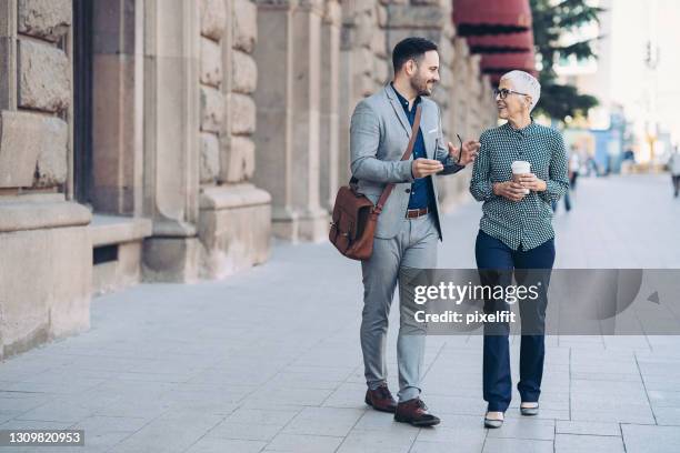 senior businesswoman and young businessman walking side by side - crossbody bag stock pictures, royalty-free photos & images