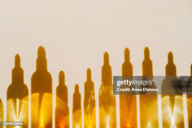 set of many different glass bottles with cosmetic liquids placed in a row on pastel beige surface. play of light creates abstract patterns from shadows and illuminating yellow reflections. trendy colors of the year 2021. flat lay style with copy space - cosmétique photos et images de collection