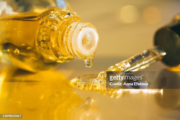 drops of bright yellow essential oil with air bubbles are dripping from glass bottle and pipette on ultimate gray surface. trendy colors of the year 2021. extreme close-up and front view - argan oil stock-fotos und bilder