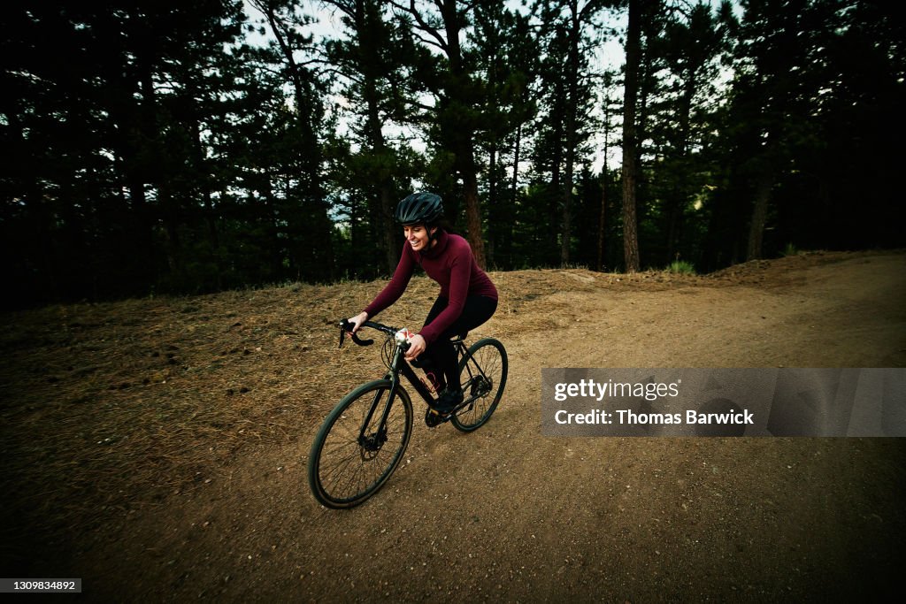 Wide shot of female athlete on evening gravel bike ride on forest road
