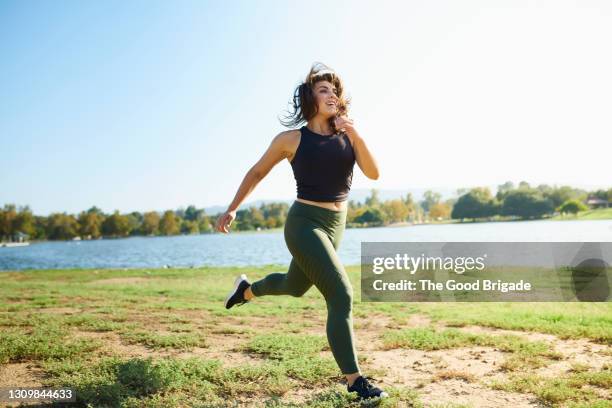 smiling young woman jogging near lake on sunny day - woman summer sport outside fotografías e imágenes de stock