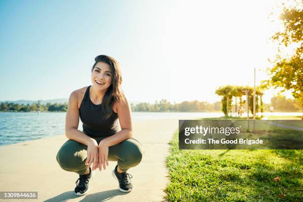 portrait of smiling young woman crouching on path by lake - agacharse fotografías e imágenes de stock