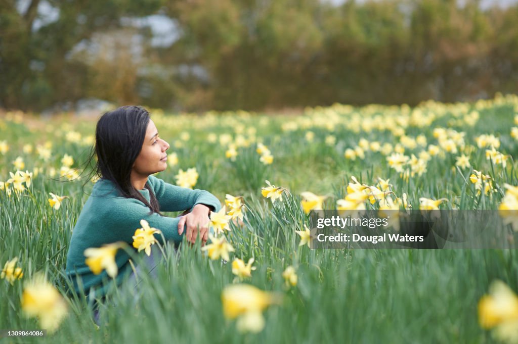 Happy Asian woman in countryside amongst wild daffodil flowers.