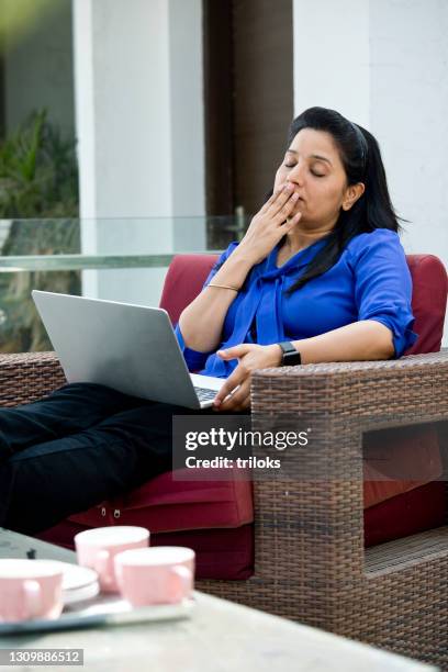woman yawning while using laptop on armchair - couch potato stock pictures, royalty-free photos & images
