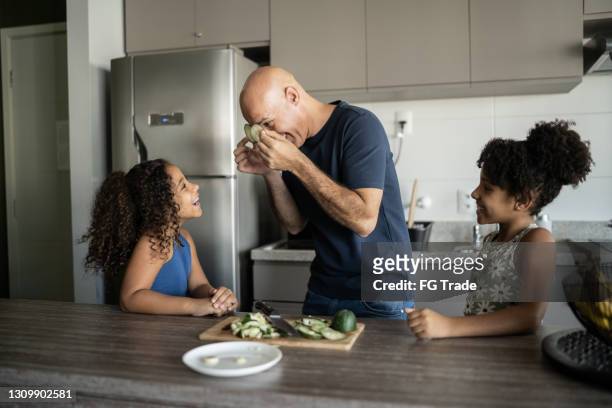 pai e filhas brincando na cozinha com fatias de pepino - pai dono de casa - fotografias e filmes do acervo