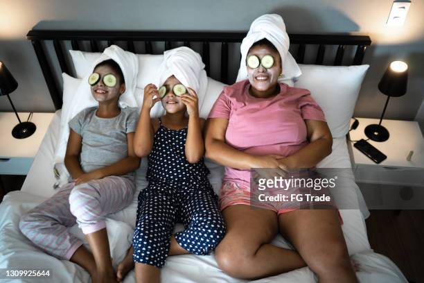 morther e figlie a letto che fanno la cura della pelle con fette di cetriolo sugli occhi - attività del fine settimana foto e immagini stock