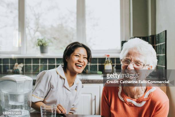 an elderly woman laughs beside a friendly young care assistant - support stock-fotos und bilder