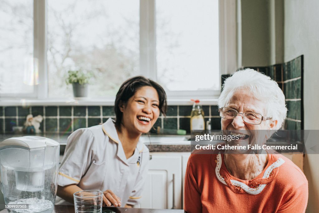 An elderly woman laughs beside a friendly young care assistant