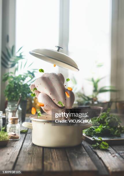 creative food composing with flying whole raw chicken , cooking pot and other flying ingredients on rustic kitchen table at window. - chicken ingredient stock pictures, royalty-free photos & images