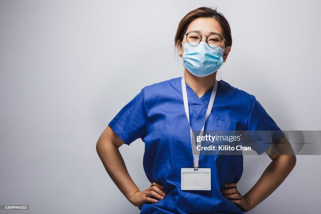 Portrait of smiling asian female doctor wearing face mask with hands on hip