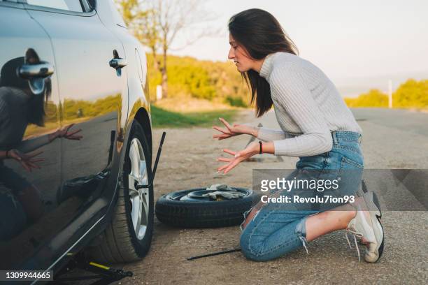 joven desesperada tratando de cambiar una llanta pinchada con hierro de neumáticos en la carretera - flat tire fotografías e imágenes de stock