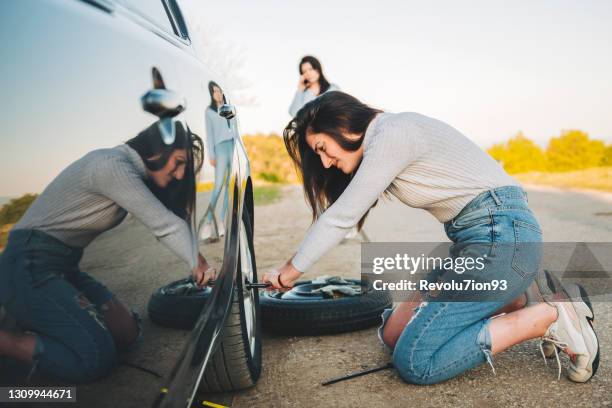 desperate young woman trying to change a flat tire with tire iron on the road - flat tyre stock pictures, royalty-free photos & images