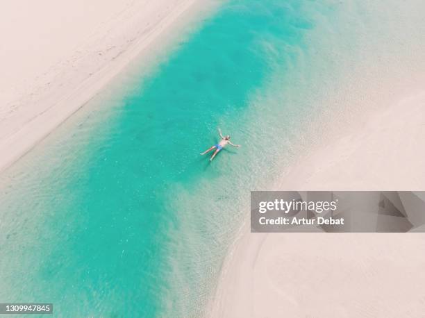 drone view of a guy floating in the turquoise lagoons in the paradise beach of fuerteventura island. spain. flotando a vista de dron en las lagunas de la playa de sotavento en fuerteventura. - canary fotografías e imágenes de stock