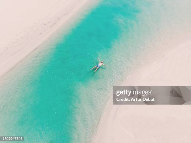 drone view of a guy floating in the turquoise lagoons in the paradise beach of fuerteventura island. spain. flotando a vista de dron en las lagunas de la playa de sotavento en fuerteventura. - en la playa ストックフォトと画像