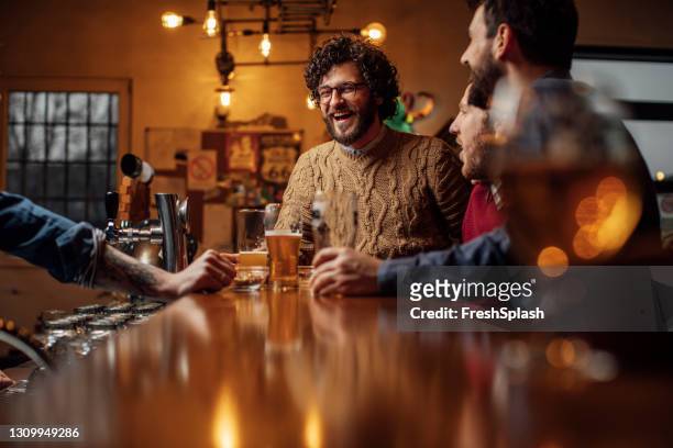 groupe d’hommes heureux buvant la bière au bar - beer bar photos et images de collection