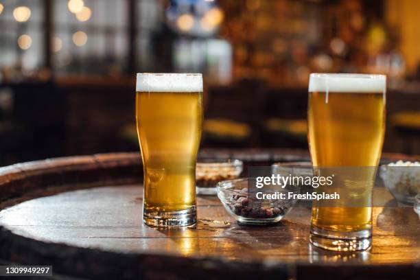 vasos de cerveza y cacahuetes en una mesa de madera en un pub, un primer plano - irish pub fotografías e imágenes de stock