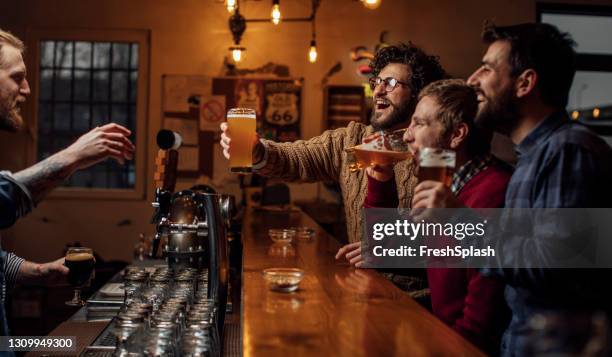 group of young guys having drinks and the bar counter, toasting with the bartender - irish pub stock pictures, royalty-free photos & images