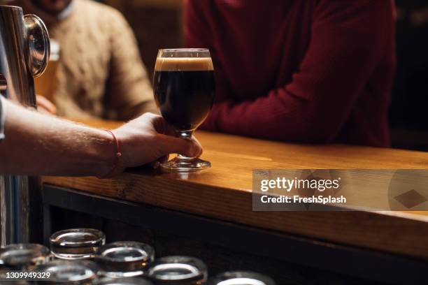 hand eines anonymen bartenders, der ein glas dunkles fassbier im pub serviert - irish pub stock-fotos und bilder