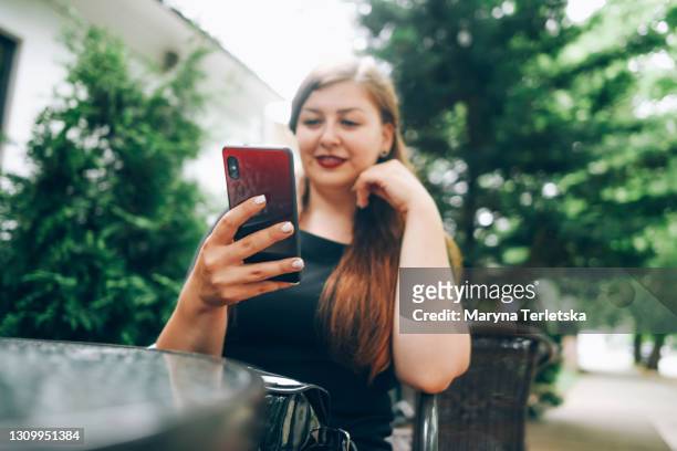 a girl in a cafe on a summer terrace looks into a smartphone. - aller plus loin photos et images de collection