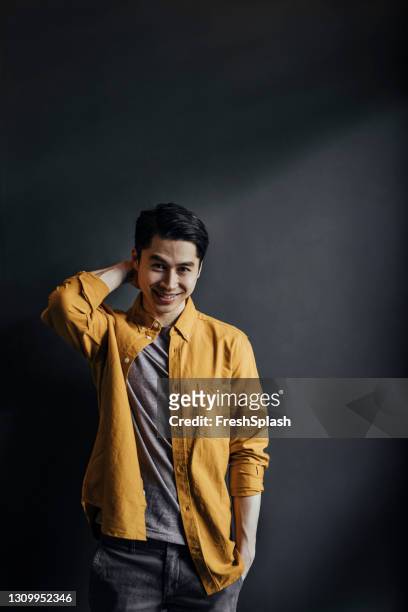 portrait of a confident young man wearing a yellow shirt and standing against a dark background - introvert stock pictures, royalty-free photos & images