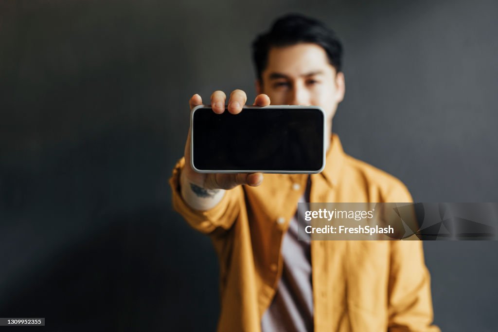 Young Handsome Man Wearing a Yellow Shirt, Showing his Smartphone Screen to the Camera