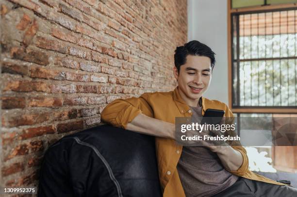 glad asiatisk student sitter i soffan och sms:ar på sin mobiltelefon - män i 30 årsåldern bildbanksfoton och bilder