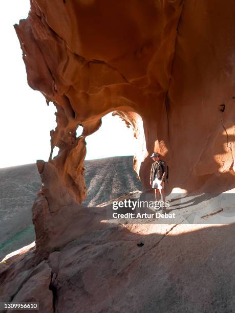 man contemplating beautiful rock formations with natural arch in fuerteventura island. spain. el arco de las peñitas en fuerteventura uno de los sitios mas instagrameables. - fuerteventura stock-fotos und bilder