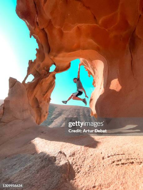 man jumping in front beautiful rock formations with natural arch in fuerteventura island. spain. el arco de las peñitas en fuerteventura uno de los sitios mas famosos de instagram. - verwonderingsdrang stockfoto's en -beelden