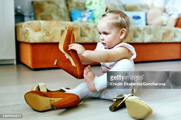 a beautiful 2-year-old girl with blonde hair  trying on mother's high-heeled shoes - free tiny girls stock-fotos und bilder