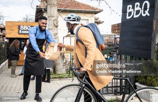 a male cyclist receives his order at the curbside pickup area from a social distance in this covid-19 pandemic - restaurants open during lockdown stock pictures, royalty-free photos & images