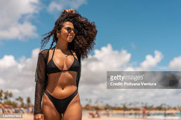 afro woman with hand in hair on the beach - beautiful black women in bathing suits stock pictures, royalty-free photos & images