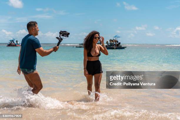 videograaf die vrouwenmodel filmt op tropisch strand - videoshoot stockfoto's en -beelden