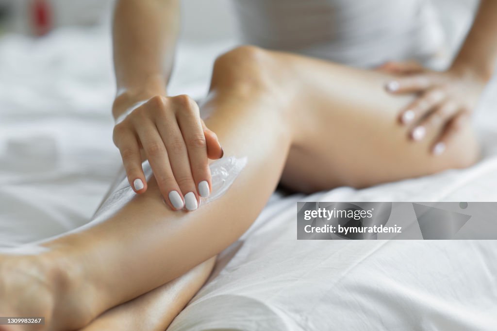 Femme appliquant la lotion de corps sur ses jambes à sa chambre à coucher.