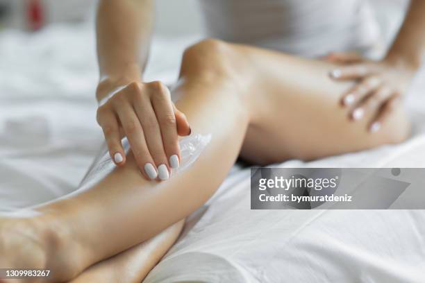 donna che applica lozione per il corpo sulle gambe nella sua camera da letto. - parte del corpo umano foto e immagini stock