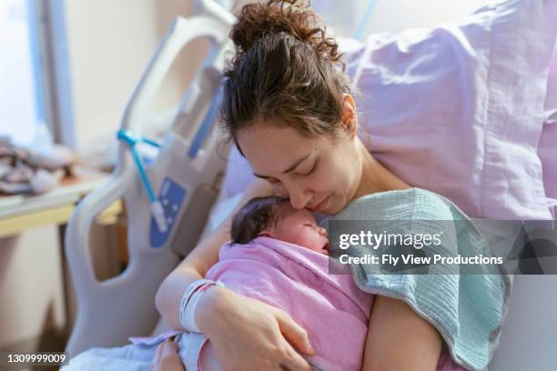 mixed race mother snuggling newborn after delivery - family photo in the delivery room stock pictures, royalty-free photos & images