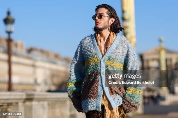 Andree Dubois wears sunglasses, a blue green and brown striped wool oversized cardigan from Y-Project, a beige and brown scarf with printed...